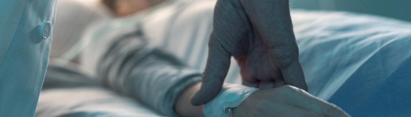 An aide comforts a patient as he lies in bed