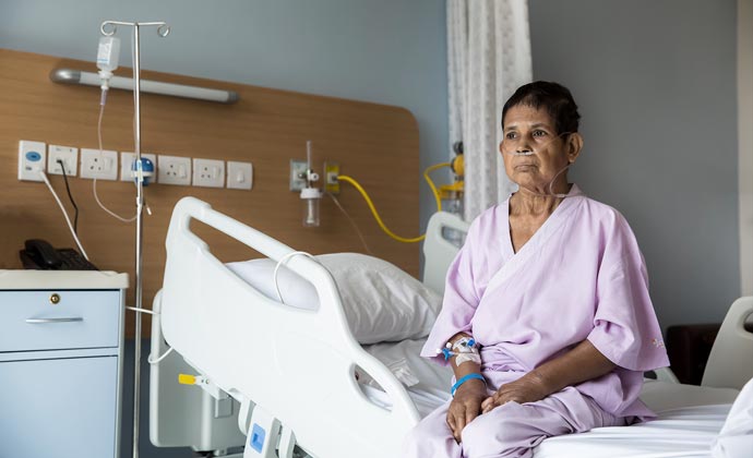 Un mujer mayor con una cánula nasal está sentada en una cama de hospital
