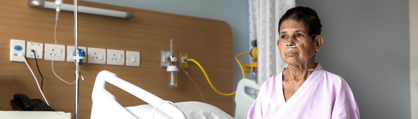 Un mujer mayor con una cánula nasal está sentada en una cama de hospital