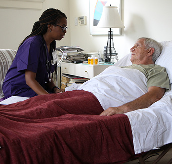 VITAS provider talks with a man lying in bed and using breathing tubes