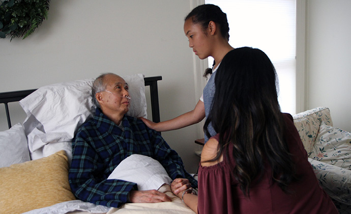 Một người đàn ông ngồi trên giường ở nhà đang nói chuyện với hai đứa cháu của mình