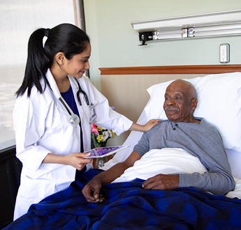 Médico de VITAS sostiene una tablet y revisa a un paciente sentado en su cama