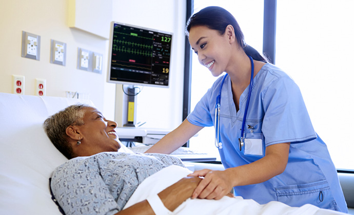 A nurse holds the hand of a patient who is lying in bed