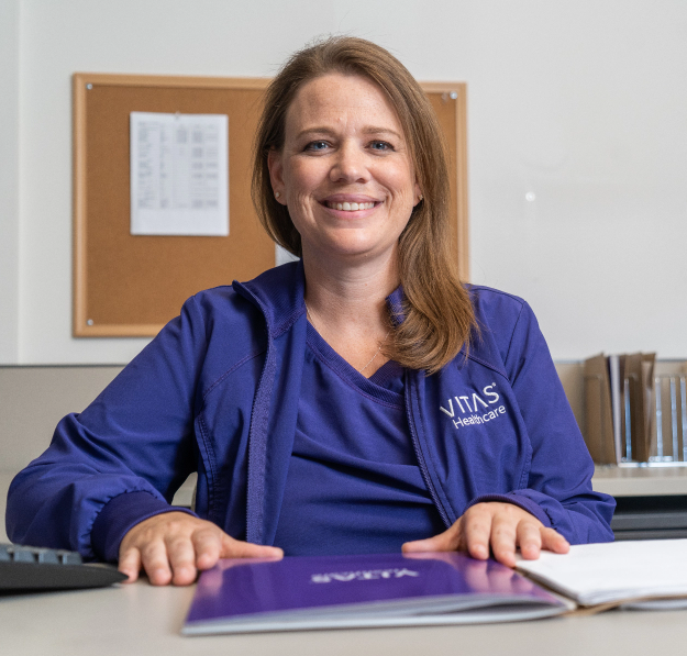 A VITAS nurse sitting at a desk with a folder in front of her