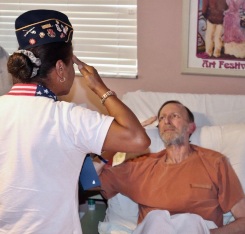 Danny Kessler, veterano del Ejército, es saludado por la gerente de voluntarios de Broward, Veronica Palomino, en presencia de familiares y cuidadores de hospicio en el domicilio del paciente.